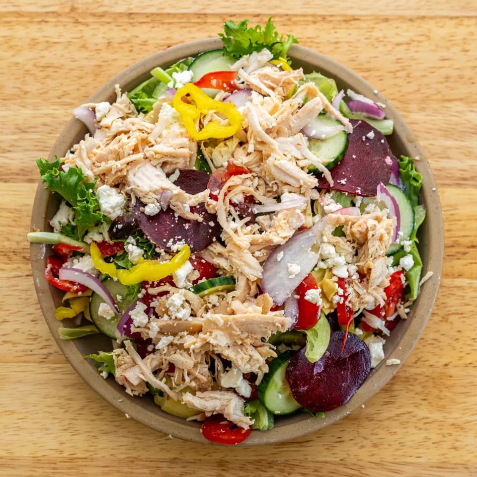 A vibrant salad with shredded chicken, feta, beets, cucumbers, and peppers in a bowl.