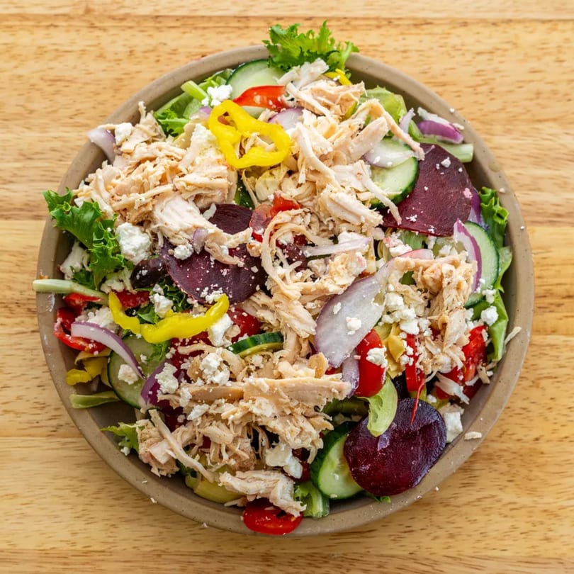 A vibrant salad with shredded chicken, feta, beets, cucumbers, and peppers in a bowl.