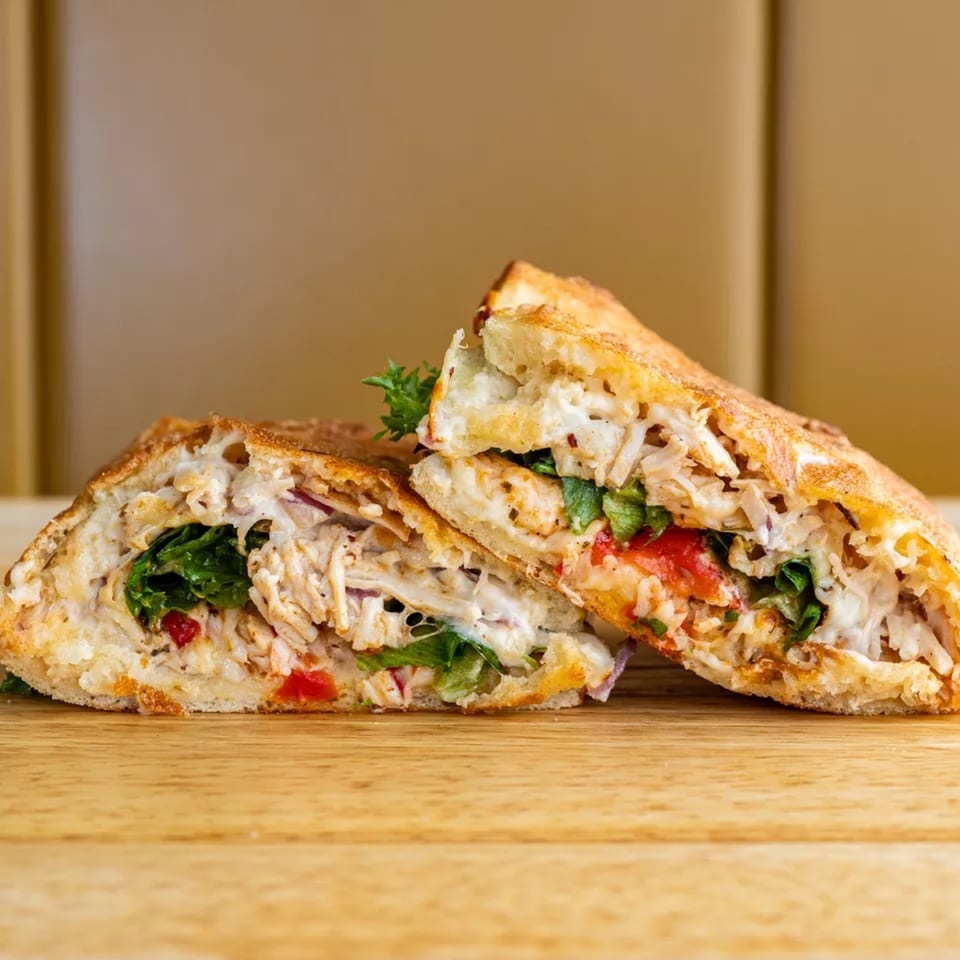 Two halves of a chicken sandwich, filled with shredded chicken, melted cheese, lettuce, and tomatoes.