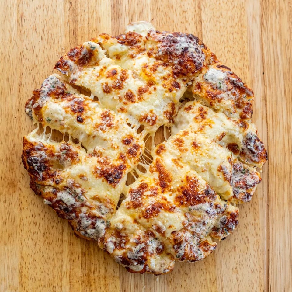 Cheesy garlic bread, golden brown and bubbling, with melted cheese strings on a wooden board.